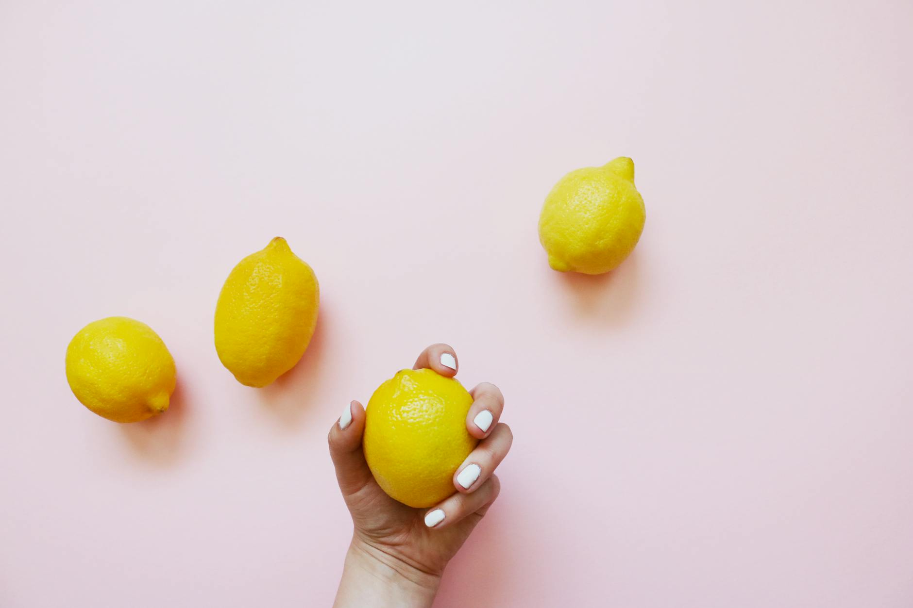 A hand holding fresh lemons on a soft pink background, symbolizing natural solutions to dryness