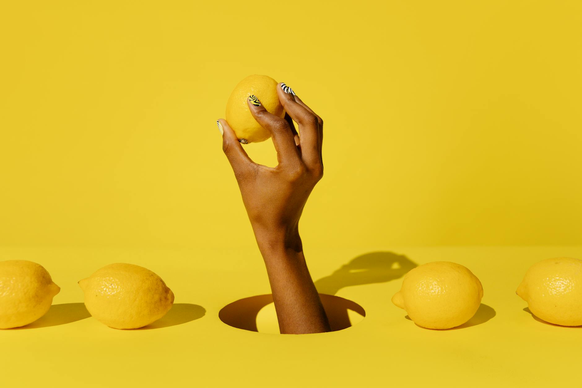 A hand holding a lemon against a vivid yellow background, symbolizing fresh starts and gentle renewal