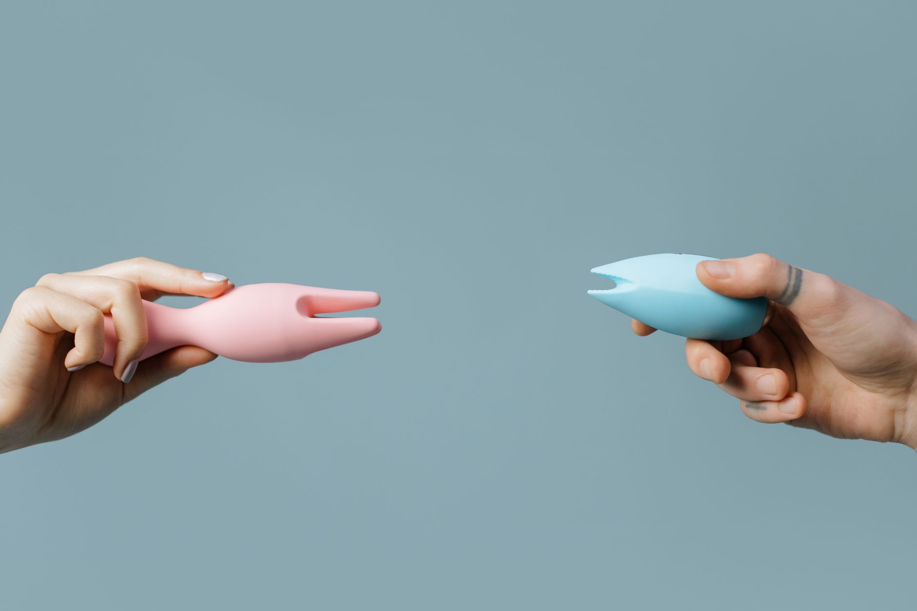 Eine Hand mit weißen Nägeln hält eine Zitrone vor rosa-hellblauem Hintergrund.