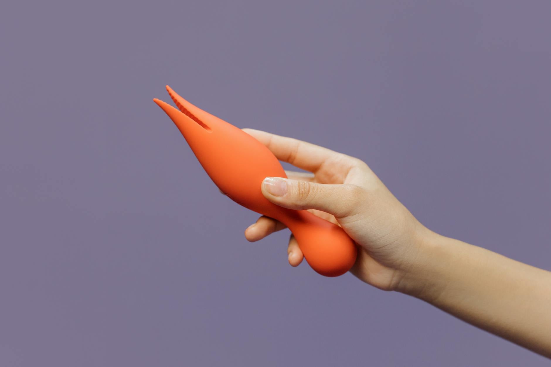 Close-up of a hand holding a lemon-colored clitoral vibrator against a minimalist purple backdrop