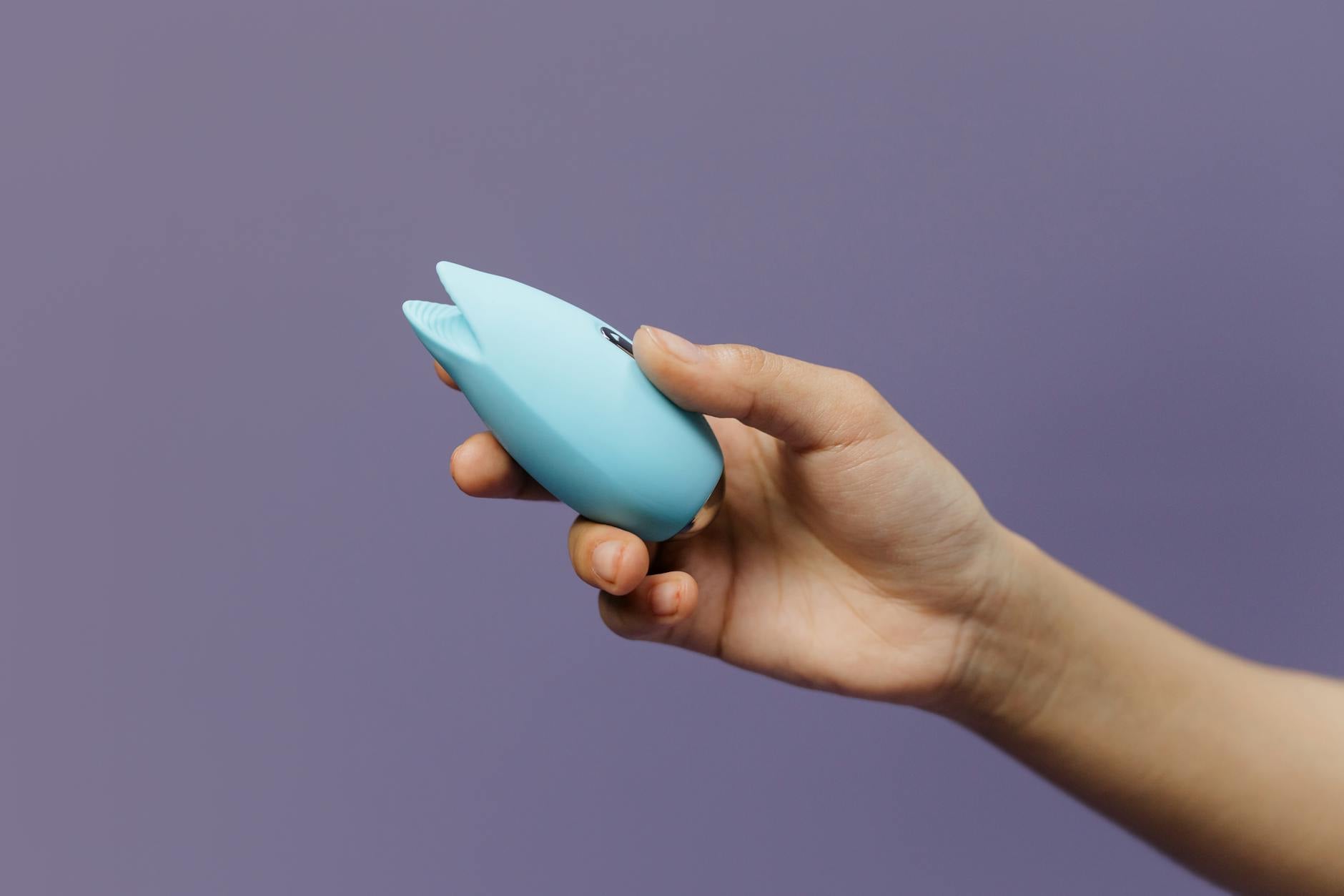 Ein blauer Silikonvibrator in der Hand gegen violetten Hintergrund, zur Förderung von Selbstliebe und Sexualität
